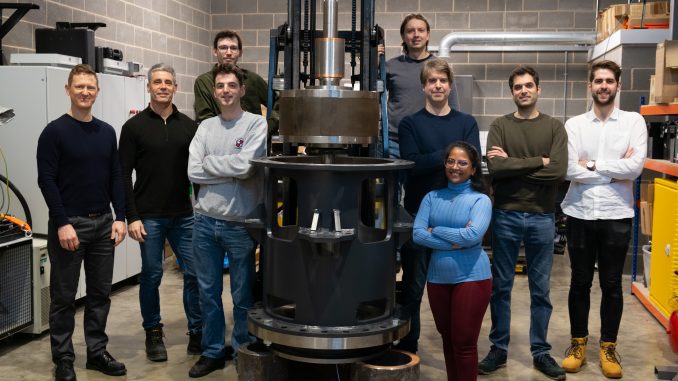 The Levistor team in 2022 posing as a group next to their flywheel technology in an industrial laboratory setting.